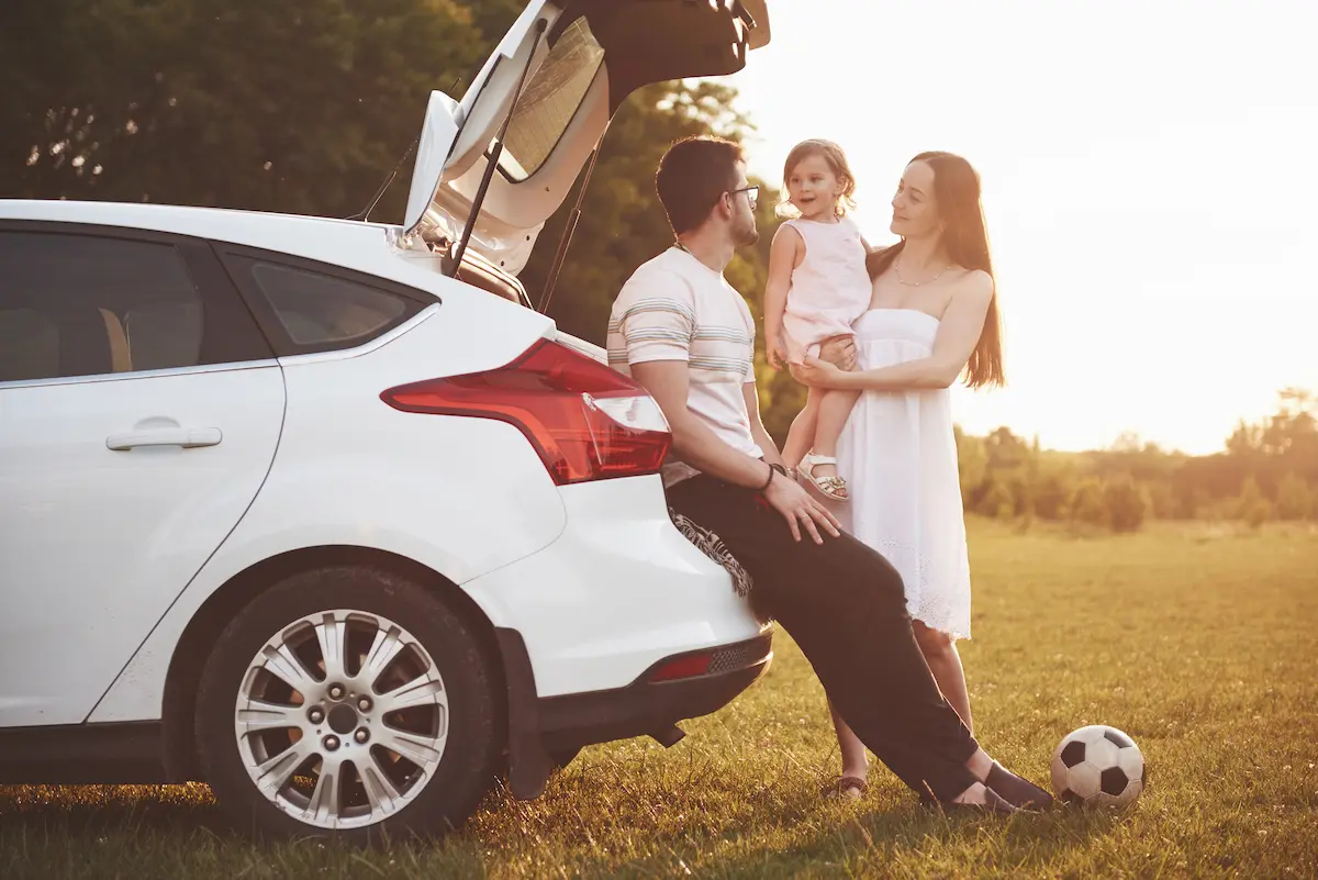 Young couple with their daugther posing behind their new car.